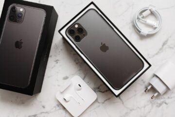 From above composition of black smartphone in box and box top and usb wire and wireless earphones on marble surface