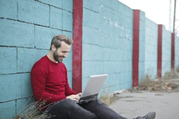 Man Leaning Against Wall Using Laptop